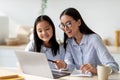 Happy asian mom helping her studying daughter, looking at laptop screen together, sitting in kitchen interior Royalty Free Stock Photo