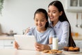 Happy asian mother and her daughter using digital tablet, looking for new recipes while sitting at kitchen, free space Royalty Free Stock Photo