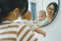 Happy Asian mother holding her little baby boy looking at their faces in mirror, Young Mom playing with her son Royalty Free Stock Photo