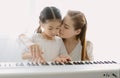 Happy Asian mother kissing and hugging her daughter while playing a piano in living room at home. Spending time at home. Moments Royalty Free Stock Photo