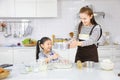 Happy Asian mother teaching her young daughter to bread baking in white modern kitchen while sieving wheat flour