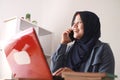 Happy Asian muslim businesswoman female entrepreneur making business phone call while working at home