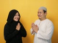 Happy Asian muslim couple doing greeting gesture, apologize and forgiving each other on eid mubarak tradition, against yellow