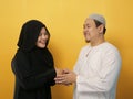 Happy Asian muslim couple doing greeting gesture, apologize and forgiving each other on eid mubarak tradition, against yellow