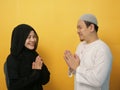 Happy Asian muslim couple doing greeting gesture, apologize and forgiving each other on eid mubarak tradition, against yellow