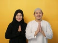 Happy Asian muslim couple making greeting gesture, hands raised up, Islamic culture