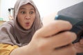 Happy Asian muslim woman excited to play games on her smart phone, close up wide angle image