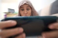 Happy Asian muslim woman excited to play games on her smart phone, close up wide angle image