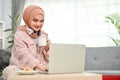 Happy Asian Muslim woman sipping coffee while using her laptop, working from home Royalty Free Stock Photo