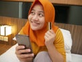 Happy Asian muslim woman wearing hijab smiling and laughing, when making purchase on online shop with her phone and credit card Royalty Free Stock Photo