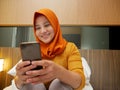Happy Asian muslim woman wearing hijab smiling when reading text message or chat on her phone while lying on bed Royalty Free Stock Photo