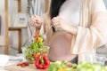 Happy asian pregnant woman cooking salad at home, doing fresh green salad, eating many different vegetables during pregnancy, Royalty Free Stock Photo