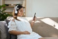 Happy Asian pregnant woman listening to music through headphones while sitting on sofa Royalty Free Stock Photo