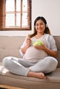 Happy Asian pregnant woman listening to music through her headphones while eating salad Royalty Free Stock Photo