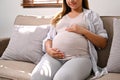 Happy Asian pregnant woman relaxes on the sofa in her living room, feeling her baby in her belly Royalty Free Stock Photo