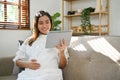 Happy Asian pregnant woman sitting on sofa, touching her belly, watching baby care on her tablet Royalty Free Stock Photo