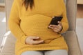 Happy Asian pregnant woman using smart phone while relaxing on sofa in her living room Royalty Free Stock Photo