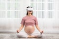 Happy Asian Pregnant woman using virtual reality glasses for practice yoga online class lotus pose to meditation smile with big Royalty Free Stock Photo