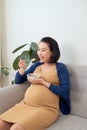 Happy Asian pregnant young woman sitting and eating fruit salad on sofa at home Royalty Free Stock Photo