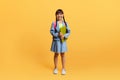 Happy asian schoolgirl with backpack and exercisebook posing on yellow Royalty Free Stock Photo