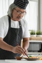 Happy Asian senior chef man holding chopsticks to meticulous arrange crushed fresh wasabi on sliced fresh salmon sashimi in plate Royalty Free Stock Photo