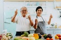 Happy Asian senior couple drinking milk at home. 70s Elderly married man and woman giving a thumbs up and holding a Royalty Free Stock Photo