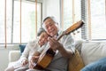 Happy Asian senior Couple enjoying singing and playing acoustic guitar together on sofa at home. Joyful Grandfather and Royalty Free Stock Photo