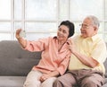 Asian senior couple having good time together,sitting in living room , talking selfie photo or video chatting looking at  smart Royalty Free Stock Photo