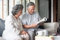 Happy Asian senior couple in love sitting on sofa reading a book together at home Royalty Free Stock Photo