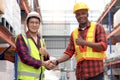 Happy Asian senior supervisor wearing safety vest and helmet, shaking hands with his colleague worker at cargo logistics warehouse Royalty Free Stock Photo