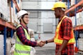 Happy Asian senior supervisor wearing safety vest and helmet, shaking hands with his colleague worker at cargo logistics warehouse Royalty Free Stock Photo