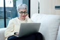 happy asian senior woman grey hair wear glasses using laptop computer sitting on couch in living room. relaxing elderly female Royalty Free Stock Photo