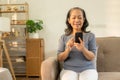 Happy Asian senior woman holding mobile phone for online video call Sitting on the sofa, Royalty Free Stock Photo