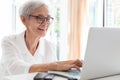 Happy asian senior woman working,surfing the internet with laptop computer at table in home,smiling elderly people in glasses with