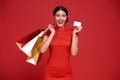 Happy Asian shopaholic woman wearing traditional cheongsam qipao dress holding credit card and shopping bag isolated on red Royalty Free Stock Photo