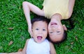 Happy asian sister and little brother lying on green grass background. Portrait of child girl and baby boy playing outdoor on lawn Royalty Free Stock Photo