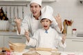 Happy Asian son kid and father in chef uniform with hat showing rock and roll finger gesture at kitchen together, dad parent and Royalty Free Stock Photo