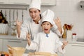 Happy Asian son kid and father in chef uniform with hat showing rock and roll finger gesture at kitchen together, dad parent and Royalty Free Stock Photo