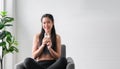 Happy Asian sports girl in sportswear sitting on chair and holding pure milk from glass after exercise in home Royalty Free Stock Photo