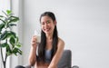 Happy Asian sports girl in sportswear sitting holding and drinking pure milk from glass after exercise in home Royalty Free Stock Photo