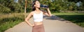 Happy asian sportswoman, runner drinks water from bottle while running, workout on fresh air in park