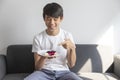 Happy Asian Teen Boy Holding Blueberry Cheesecake Cake sit on sofa at home. Royalty Free Stock Photo