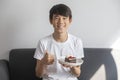 Happy Asian Teen Boy Holding Blueberry Cheesecake Cake sit on sofa at home. Royalty Free Stock Photo