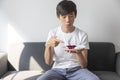 Happy Asian Teen Boy Holding Blueberry Cheesecake Cake sit on sofa at home. Royalty Free Stock Photo