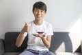 Happy Asian Teen Boy Holding Blueberry Cheesecake Cake sit on sofa at home. Royalty Free Stock Photo