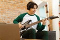 Happy Asian Teen Guy Playing Electric Guitar Using Laptop Indoor Royalty Free Stock Photo