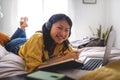 Happy asian teen student doing homework at home bedroom lying on bed looking at camera.Chinese teenage girl using laptop Royalty Free Stock Photo