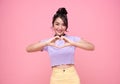 Happy asian teen woman hand showing mini heart gesture over pink background