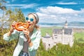 Asian traveller girl eats crispy pretzel in the background of the legendary Neuschwanstein castle. Tourism in Bavaria
