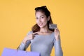 Happy Asian woman carry shopping bags and pointing at credit card smiling over yellow background, empty space Royalty Free Stock Photo